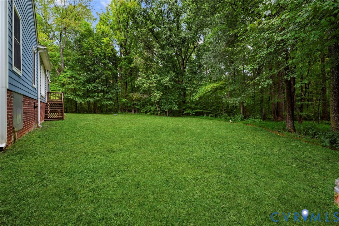 Expansive backyard featuring a level lawn, mature trees, brick and lap siding exterior, and a wooden deck. Virtually edited grass