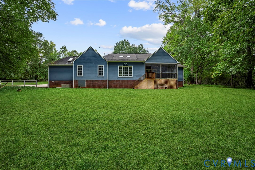 Rear exterior featuring horizontal lap siding, brick foundation, screened-in porch, skylights, and expansive lawn. Virtually edited grass