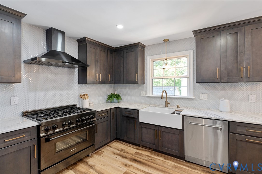 Kitchen featuring charcoal-toned shaker cabinetry, stone-finish countertops, a white farmhouse-style sink, stainless steel professional-grade range, and herringbone-pattern tile backsplash
