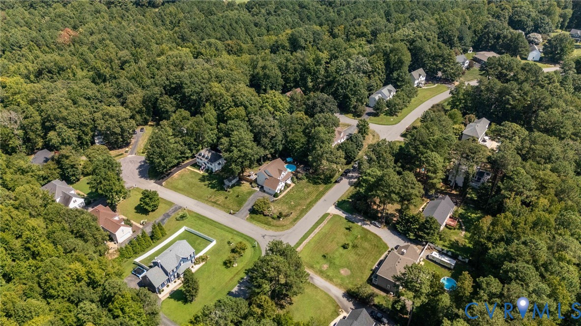 Aerial perspective of a residential neighborhood characterized by established tree canopy, paved roads, and manicured lawns