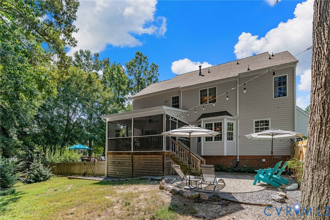 Rear exterior featuring light-toned horizontal siding, a brick foundation, a screened-in porch with wood-finish decking, and a paver stone patio