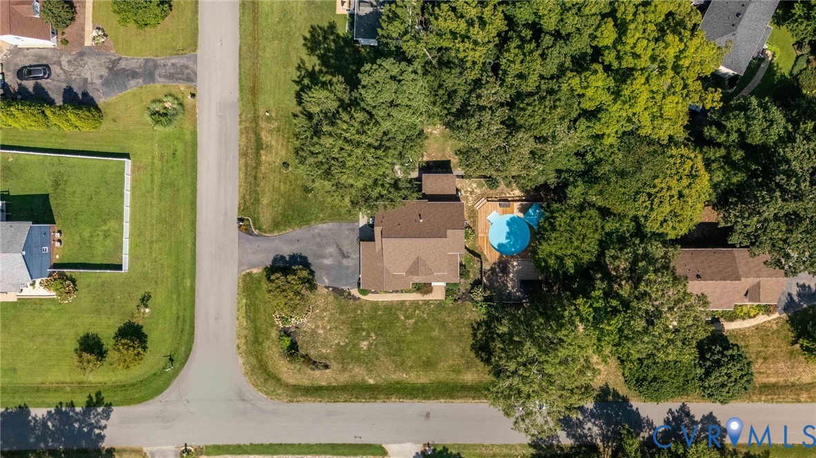 Aerial perspective of a residential property featuring an in-ground pool, expansive lawn, multi-level wood decking, and mature tree canopy