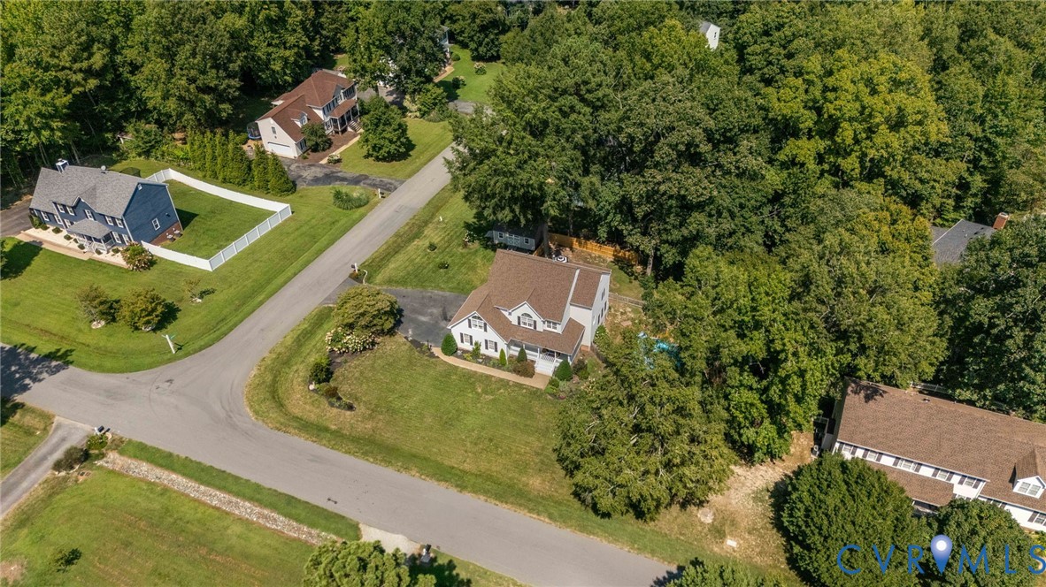 Aerial perspective of a detached residence featuring a multi-gabled roof, an asphalt driveway, and a large lot characterized by mature trees