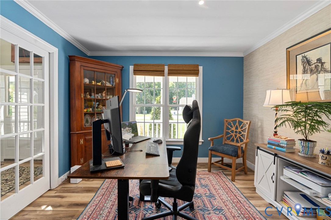 Room featuring wood-finish flooring, crown molding, a built-in corner hutch, textured wall covering, and a French-style glass pane door