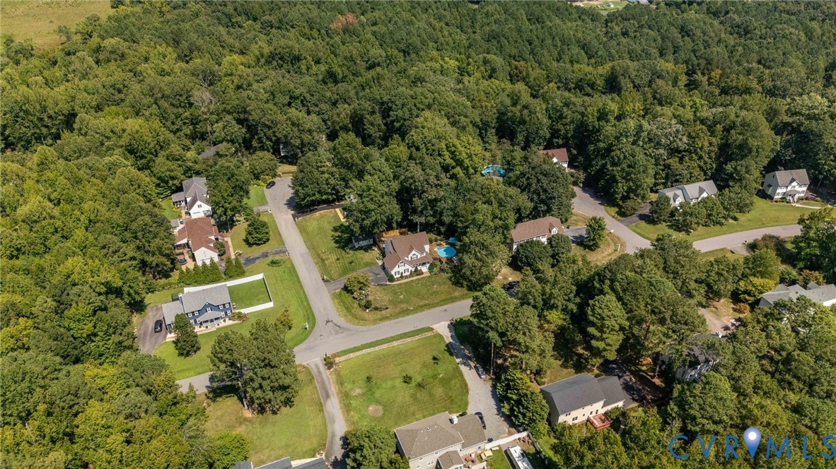 Aerial perspective of a residential neighborhood featuring paved streets, detached single-family residences, mature tree cover, and private swimming pools