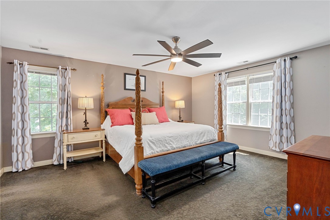 Neutral-toned walls, expansive windows with dual-rod drapery hardware, plush carpeting, and a multi-blade ceiling fan with integrated lighting