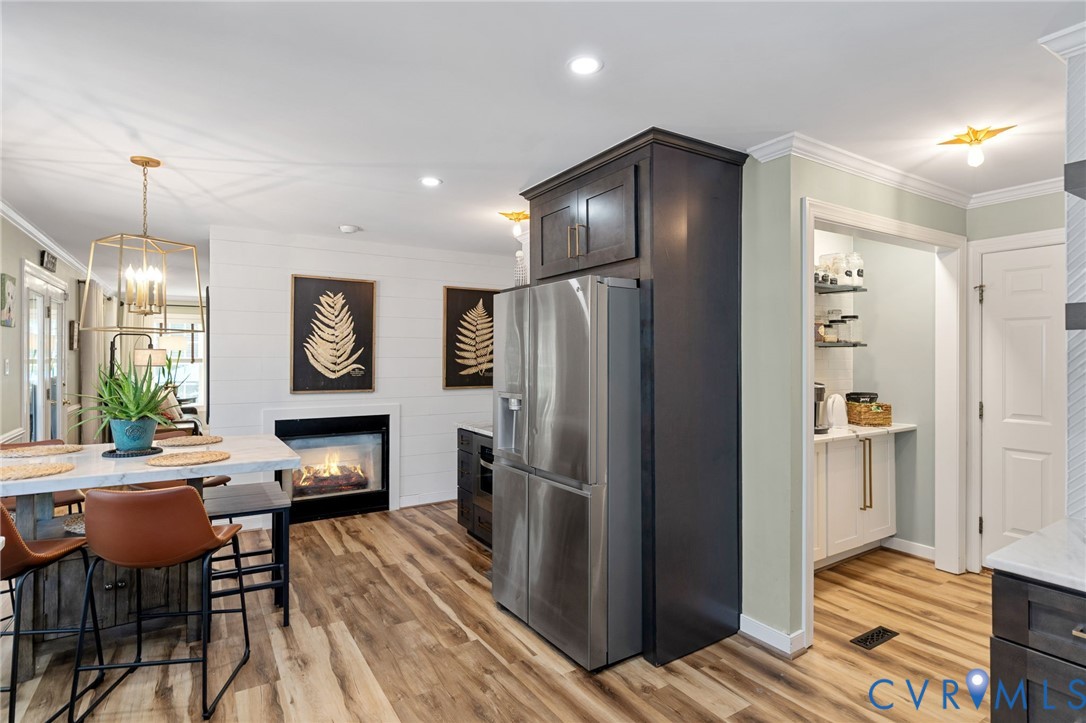 Kitchen featuring dark-finish cabinetry, stainless steel refrigerator, white plank wall detailing, inset fireplace, and wood-finish flooring