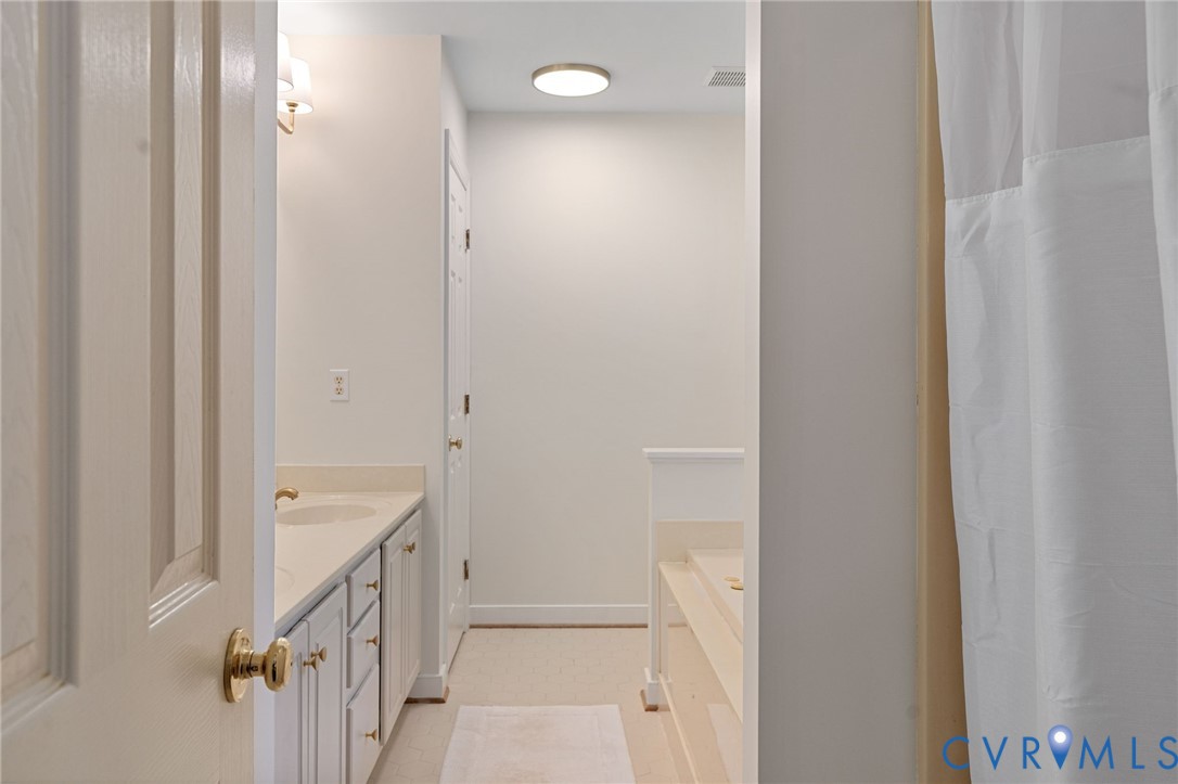 Dual-sink vanity with light-toned cabinetry, surface-mounted lighting, and a built-in tub with tile surround