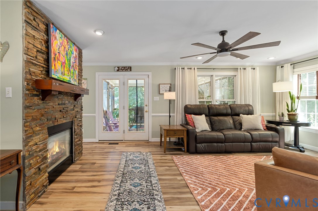 Stacked stone fireplace with a prominent wood mantel, wood-finish flooring, recessed lighting, ceiling fan, and double-door entry