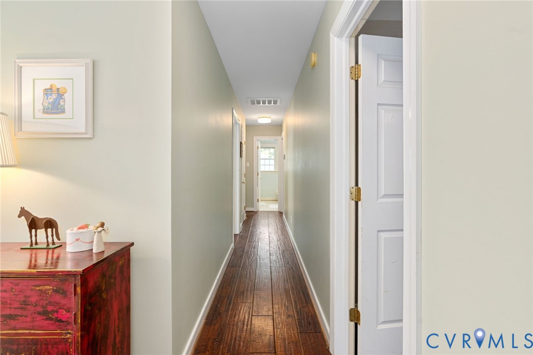 Hallway featuring wood-finish flooring, neutral wall paint, and multi-panel interior doors with brass-tone hardware