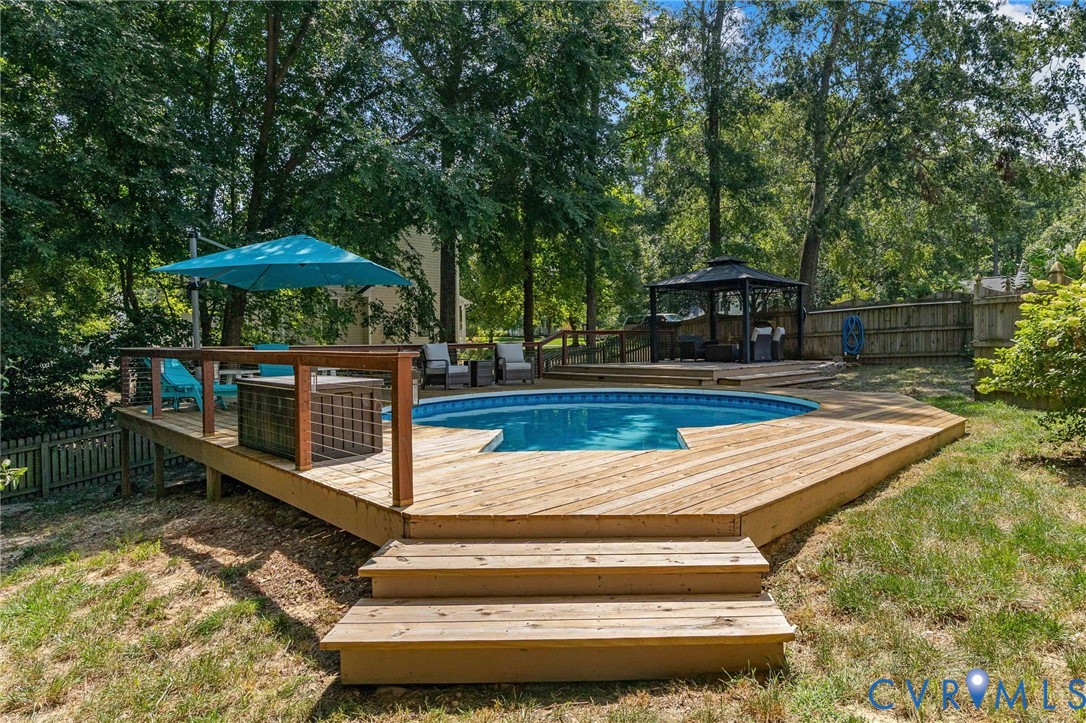 Multi-level wooden decking featuring an integrated pool, built-in staircase, wood railing, and a permanent metal-framed gazebo