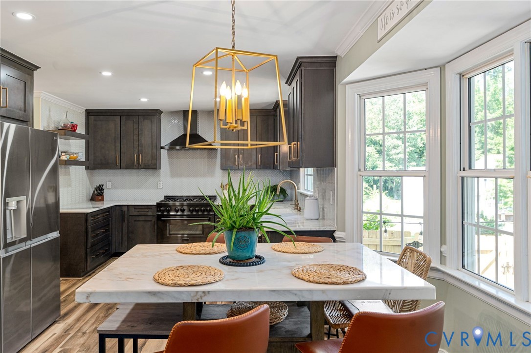 Kitchen featuring dark cabinetry, stone-surface island, metal geometric chandelier, stainless steel appliances, and bay windows