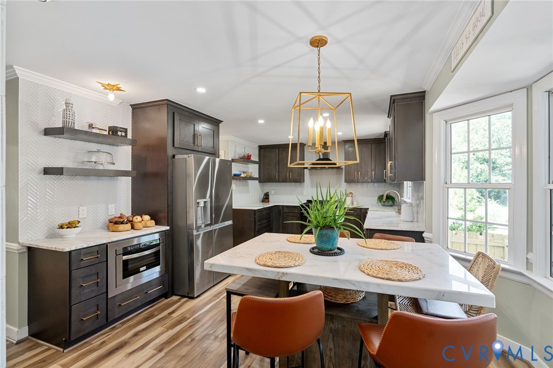 Kitchen featuring dark wood cabinetry, stainless steel appliances, stone countertops, herringbone patterned wall tile, and geometric pendant lighting