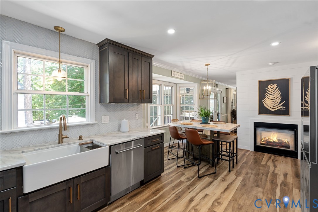 Kitchen featuring dark cabinetry, farmhouse sink, stone countertops, wood-finish flooring, and built-in fireplace