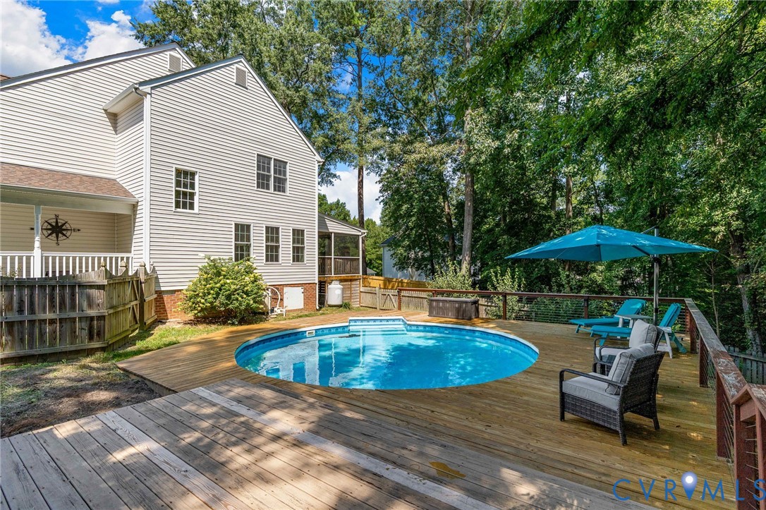 Rear exterior featuring a multi-level wood deck, an above-ground swimming pool, vinyl siding, and mature tree-lined perimeter