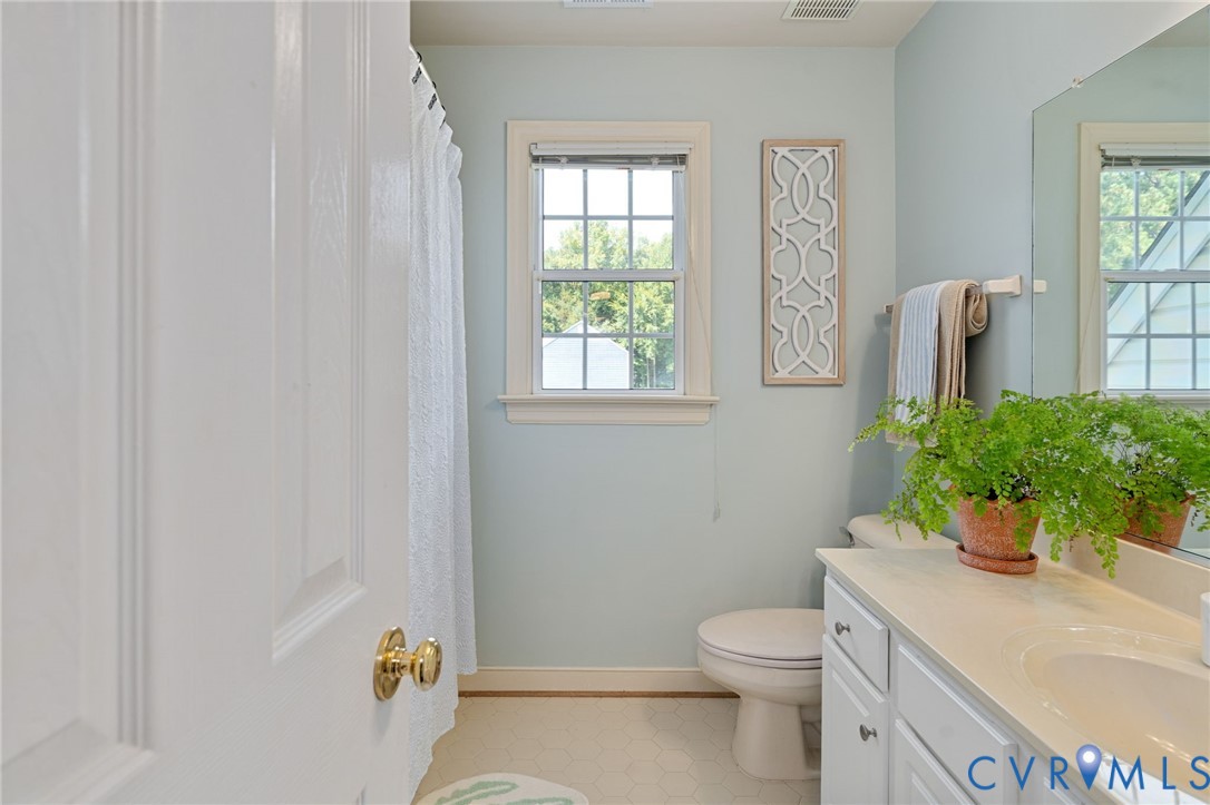Bathroom featuring a white vanity cabinet, solid-surface countertop with an integrated sink, large wall-mounted mirror, and a double-hung window