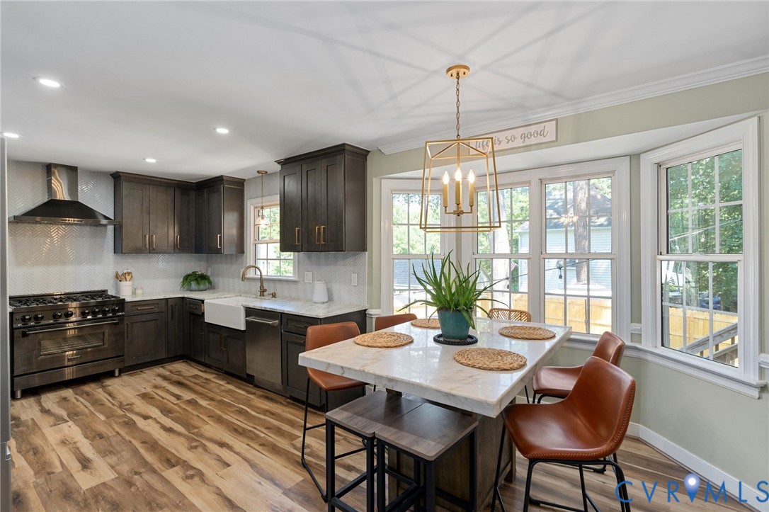 Kitchen featuring dark wood-finish cabinetry, stone countertops, farmhouse-style sink, stainless steel professional-grade range with matching hood, and wood-finish flooring