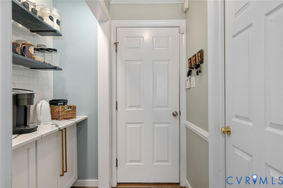 White cabinetry with gold-tone hardware, quartz countertop, subway tile backsplash, and stained wood floating shelves