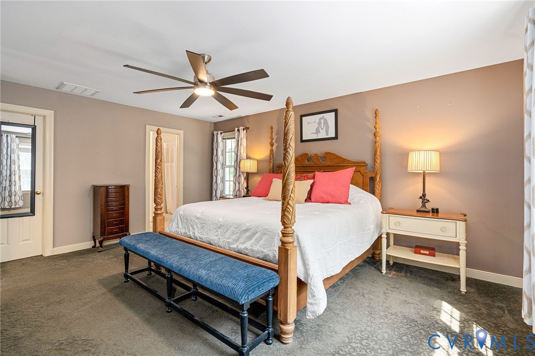 Spacious room featuring neutral wall tones, multi-tone patterned carpeting, and a multi-blade ceiling fan with integrated lighting
