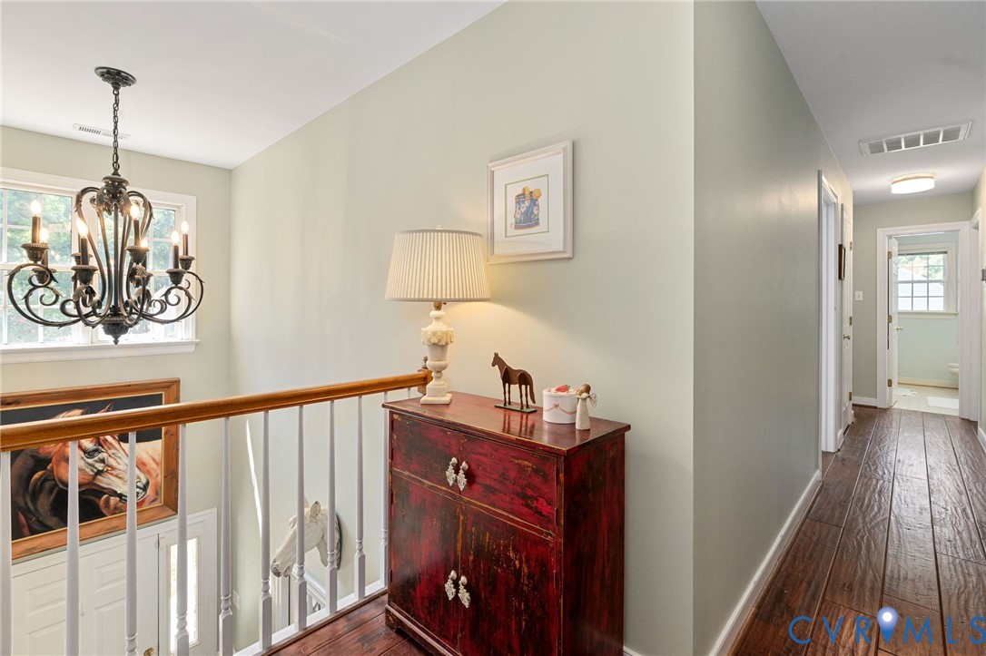Hardwood flooring, ornate metal chandelier, and wooden staircase railing with vertical balusters