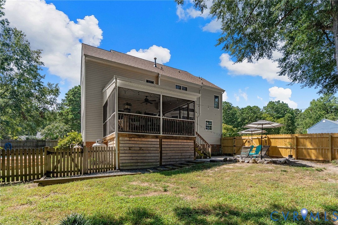 Exterior featuring a screened-in porch with ceiling fan, raised wood deck, wood privacy fencing, and stone-bordered patio area
