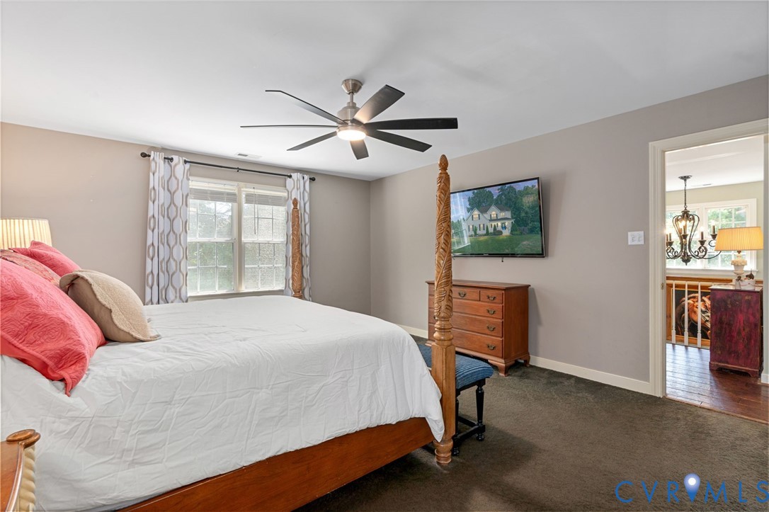 Neutral-toned interior space featuring a multi-blade ceiling fan, wall-mounted television, and dual-window assembly with integrated hardware