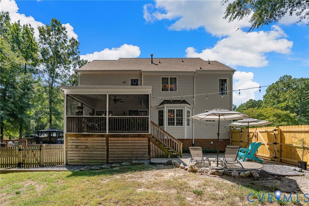Rear exterior featuring a screened porch with ceiling fan, wood-frame deck, stone-paver patio, and wood privacy fencing