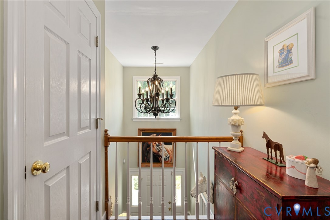 Multi-level interior featuring a decorative metal chandelier, wood-finish stair railing with vertical balusters, and multi-pane window