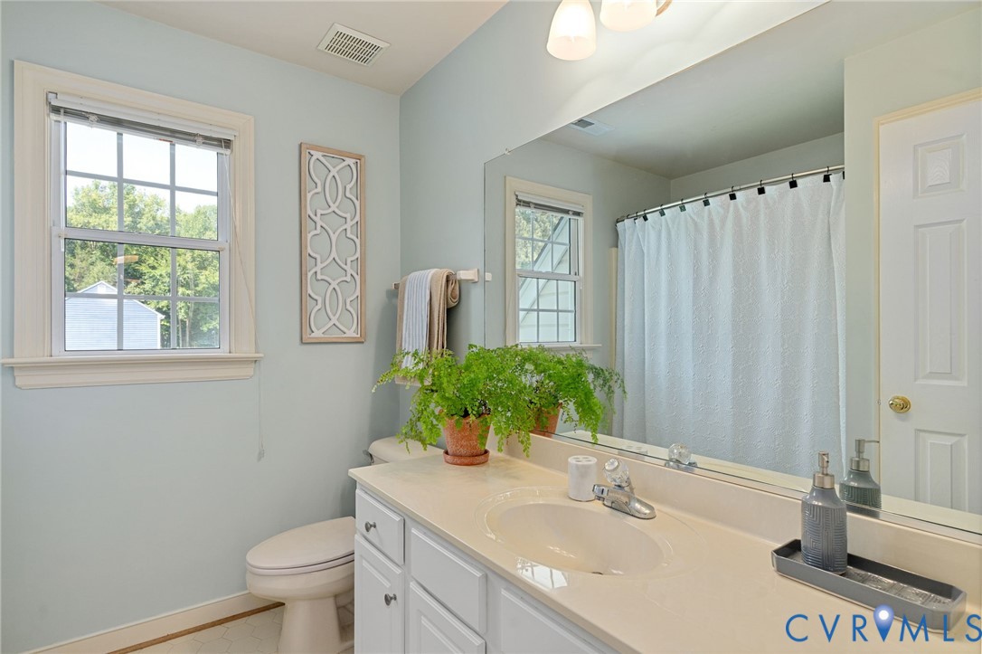 Bathroom featuring a white vanity cabinet, solid-surface countertop with an integrated basin, expansive wall-to-wall mirror, multi-pane window with wood trim, and a shower-tub combination