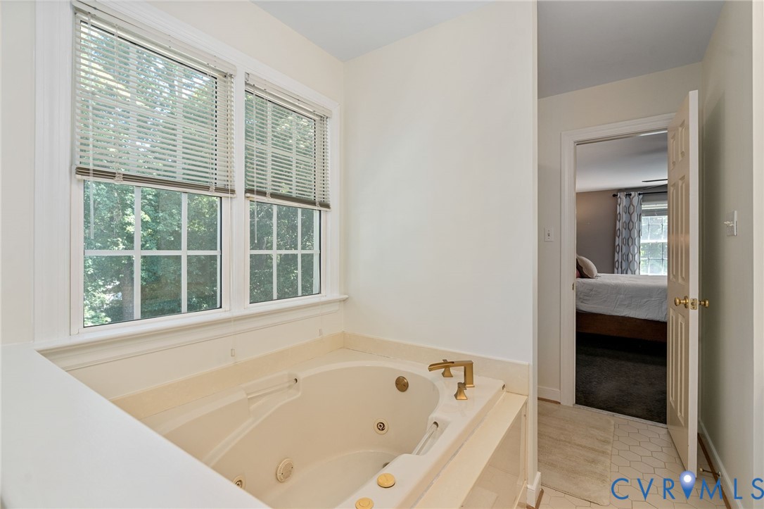 Jetted soaking tub with brass-finish hardware, surrounding stone-finish tile deck, and multi-pane windows