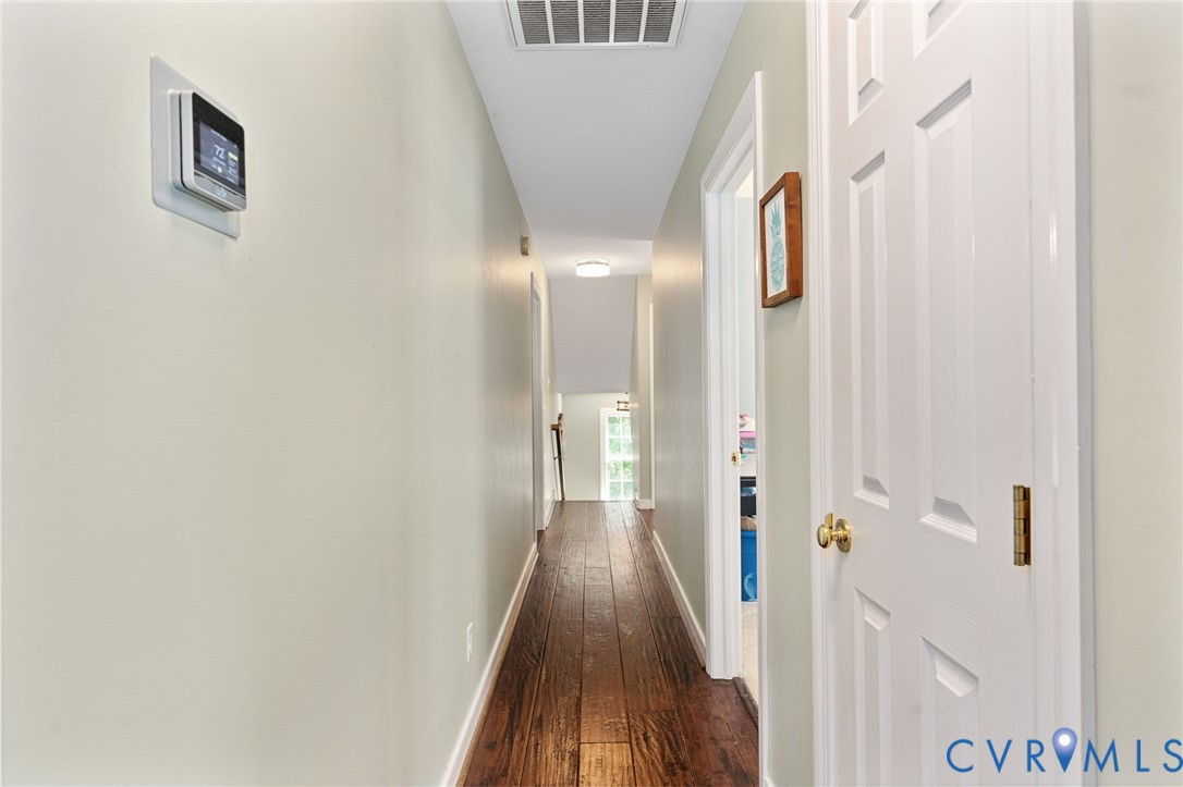 Hallway featuring dark wood-finish flooring, white paneled doors, and a digital programmable thermostat