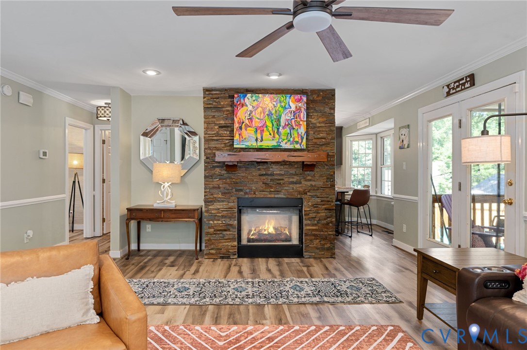 Floor-to-ceiling stacked stone fireplace with a natural wood mantel, wood-finish flooring, recessed lighting, ceiling fan, and double-door access to an exterior space