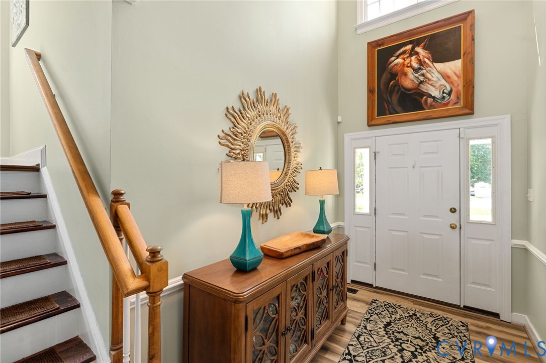 Double-height foyer featuring a multi-panel front door with sidelights, a wood-finish staircase with a turned wood railing, and upper-level transom window