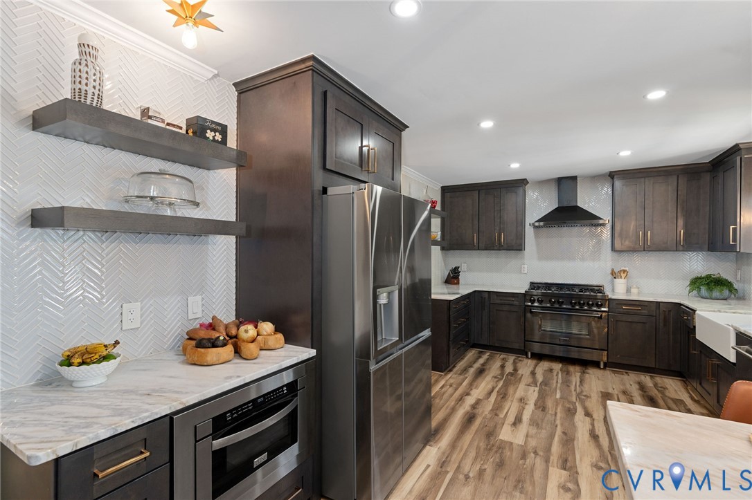 Kitchen featuring dark-finish cabinetry, stone-finish countertops, stainless steel appliances, a white farmhouse sink, and a herringbone-patterned tile backsplash