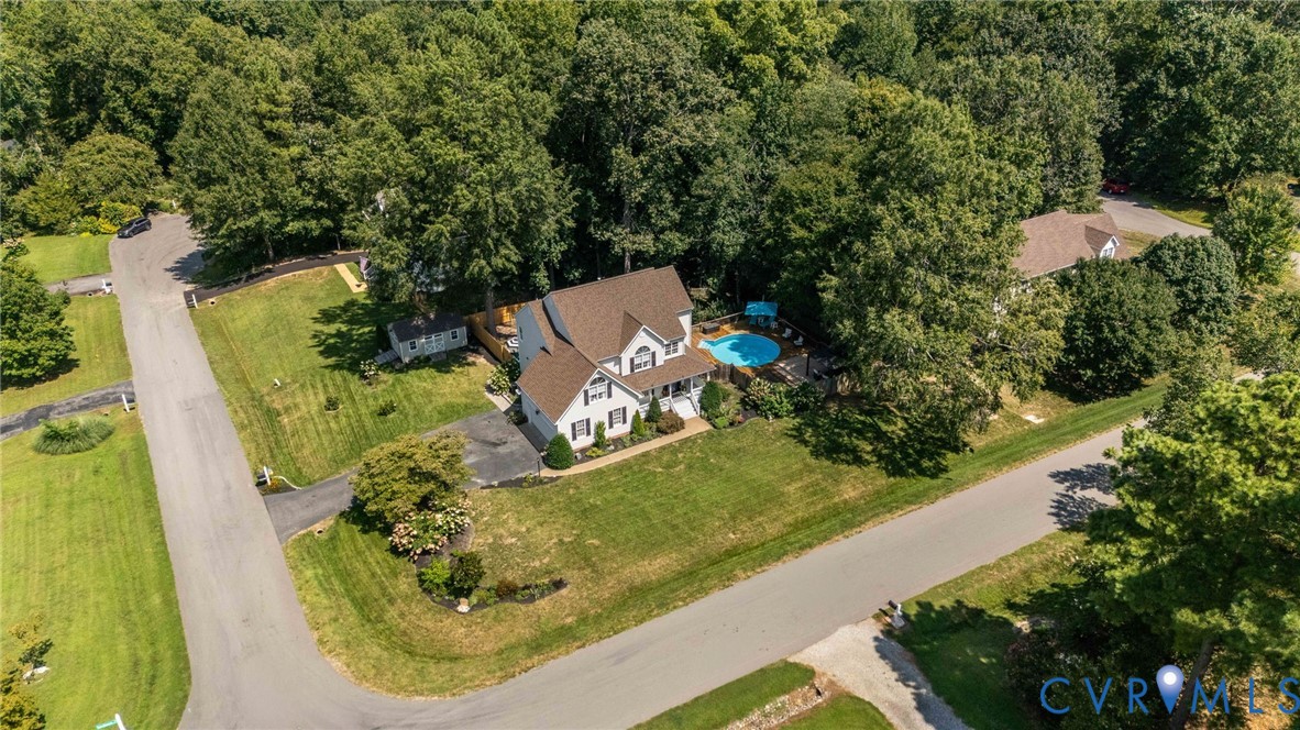 Multi-story residence featuring a shingled roof, in-ground swimming pool, asphalt driveway, and expansive lawn surrounded by mature trees