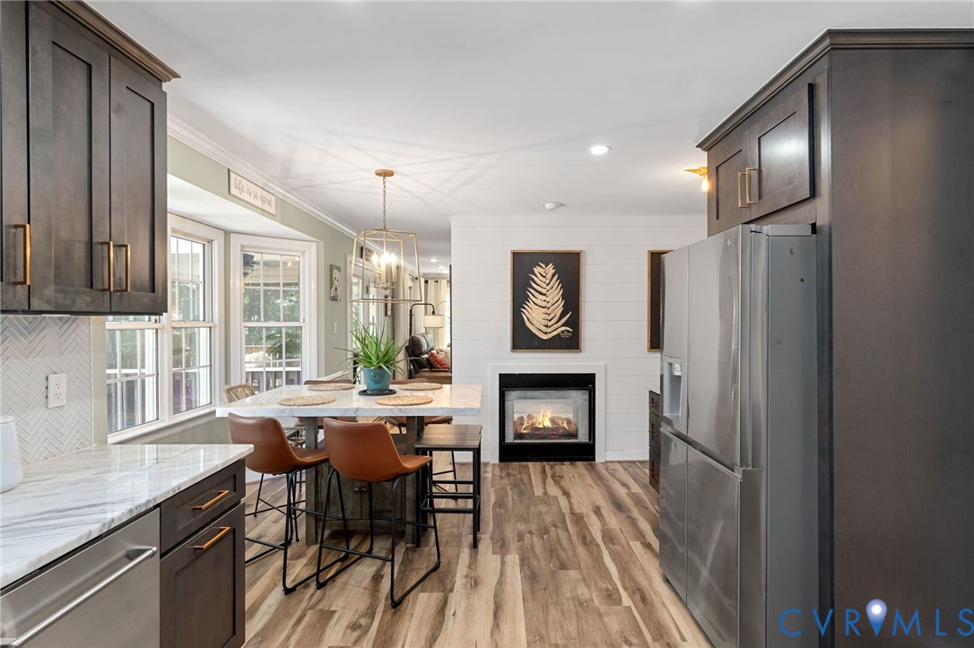 Kitchen featuring dark-finish cabinetry, stone-style countertops, stainless steel appliances, shiplap wall accents, and wood-finish flooring