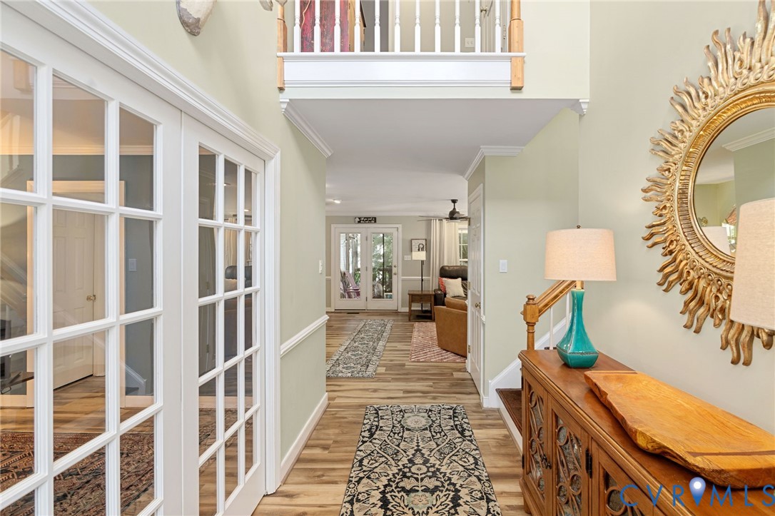 Two-story foyer featuring wood-finish flooring, white French doors, wainscoting, and a wooden staircase railing