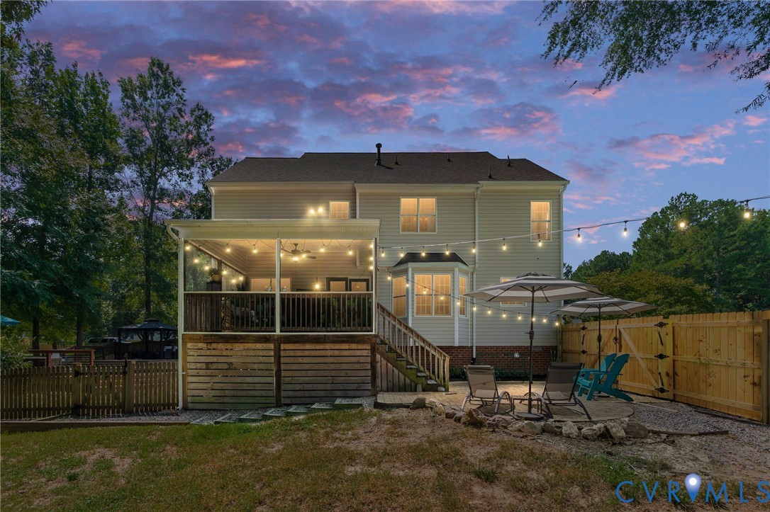 Exterior rear elevation featuring a covered back porch with a ceiling fan, a gravel patio, and wood privacy fencing