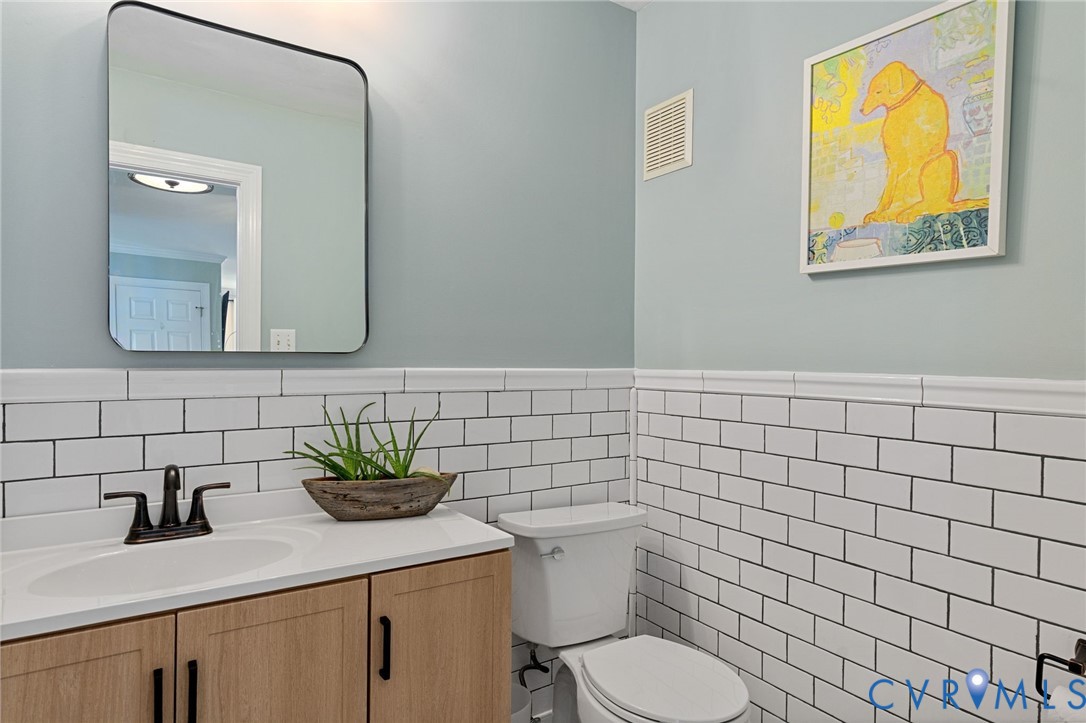 Wood-finish vanity cabinet with a white countertop, undermount sink, matte black faucet, and white subway tile wainscoting topped with a rectangular wall-mounted mirror