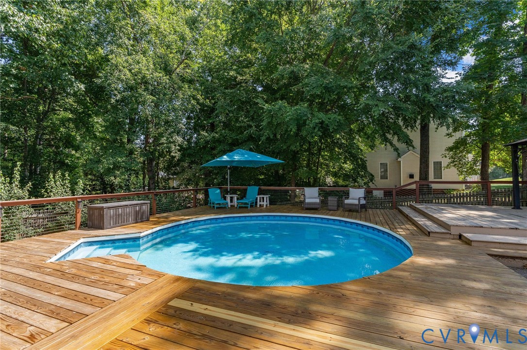 Above-ground swimming pool surrounded by tiered wood decking, cable railing system, and mature tree canopy