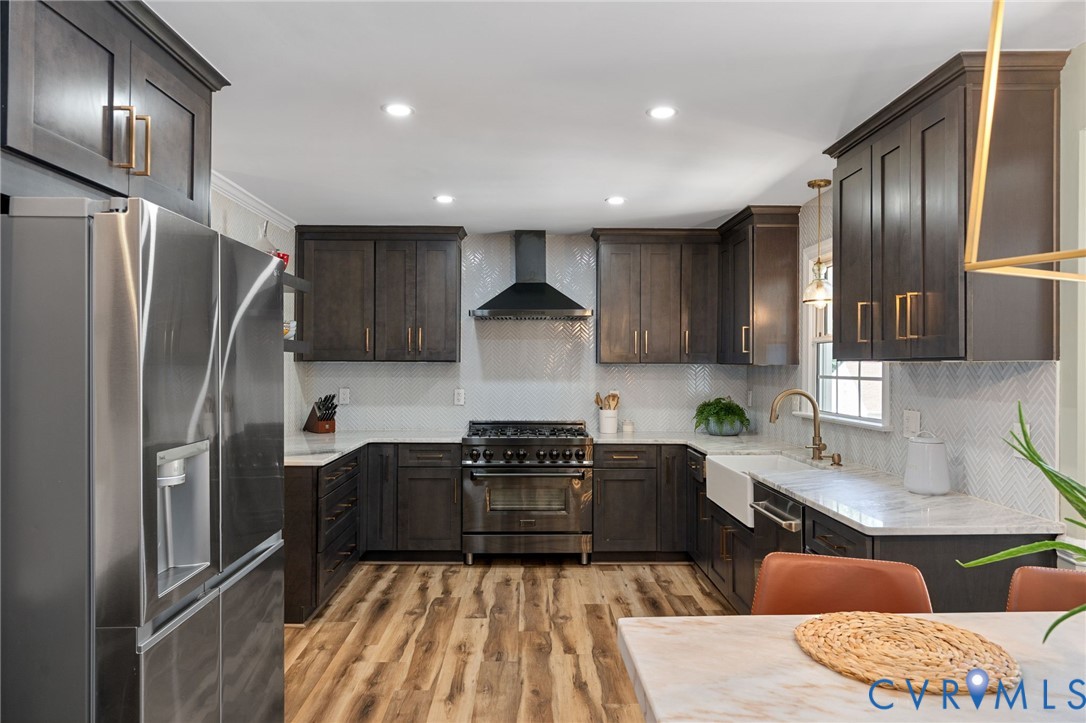 Kitchen featuring dark wood cabinetry with gold-tone hardware, a white apron-front sink, quartz countertops, a herringbone-pattern tile backsplash, and wood-finish flooring