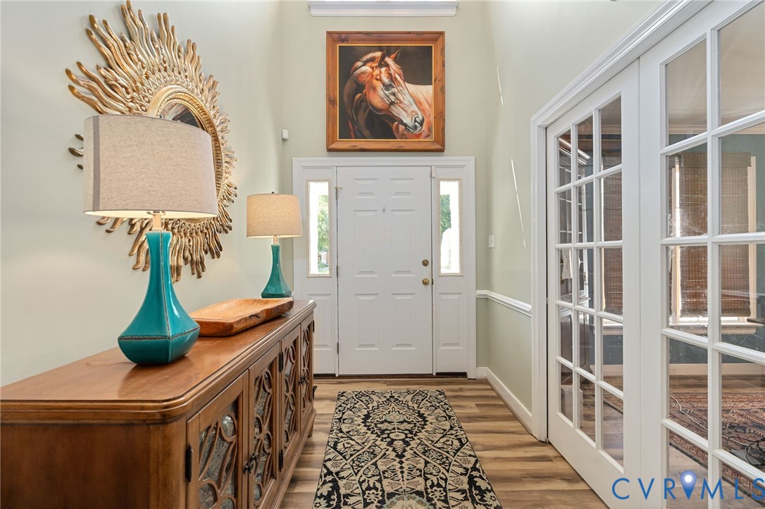 Foyer featuring high ceilings, wood-finish flooring, white paneled entry door with dual sidelights, and glass-paneled French doors