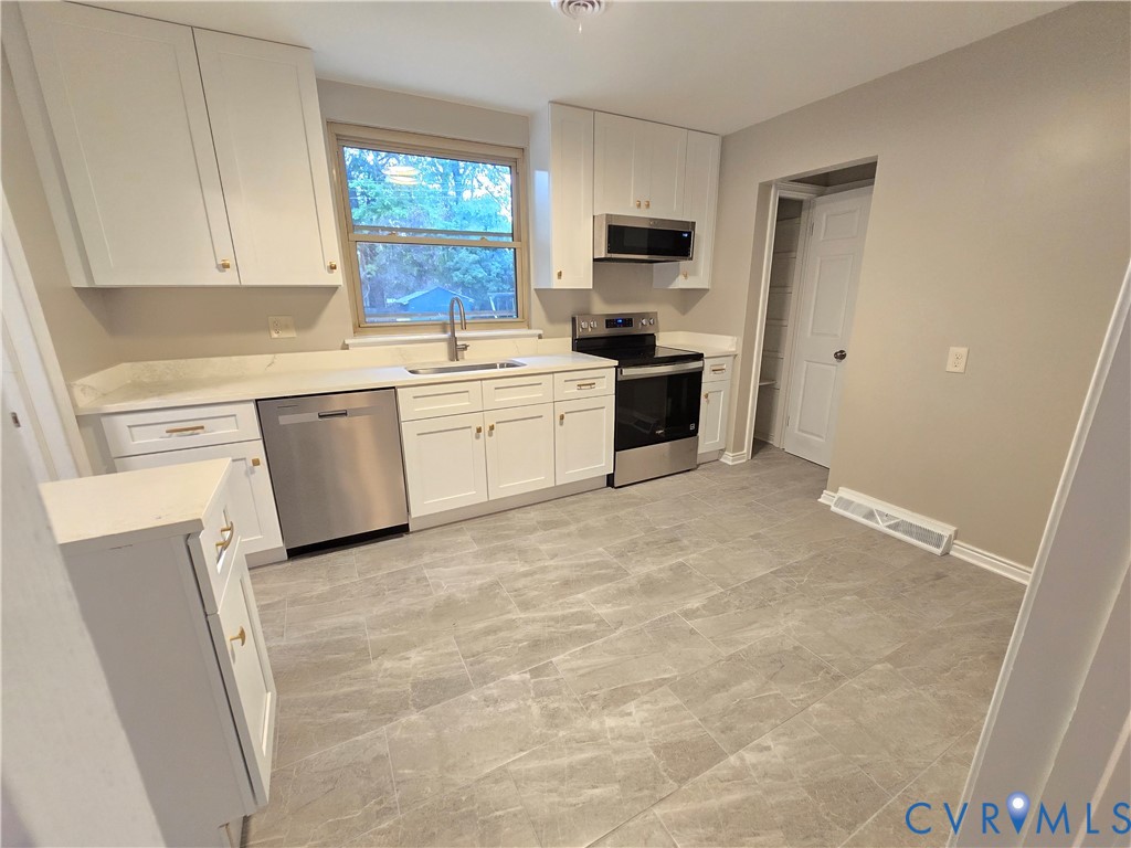 Kitchen featuring white Shaker-style cabinetry, solid-surface countertops, stone-patterned tile flooring, and stainless steel appliances