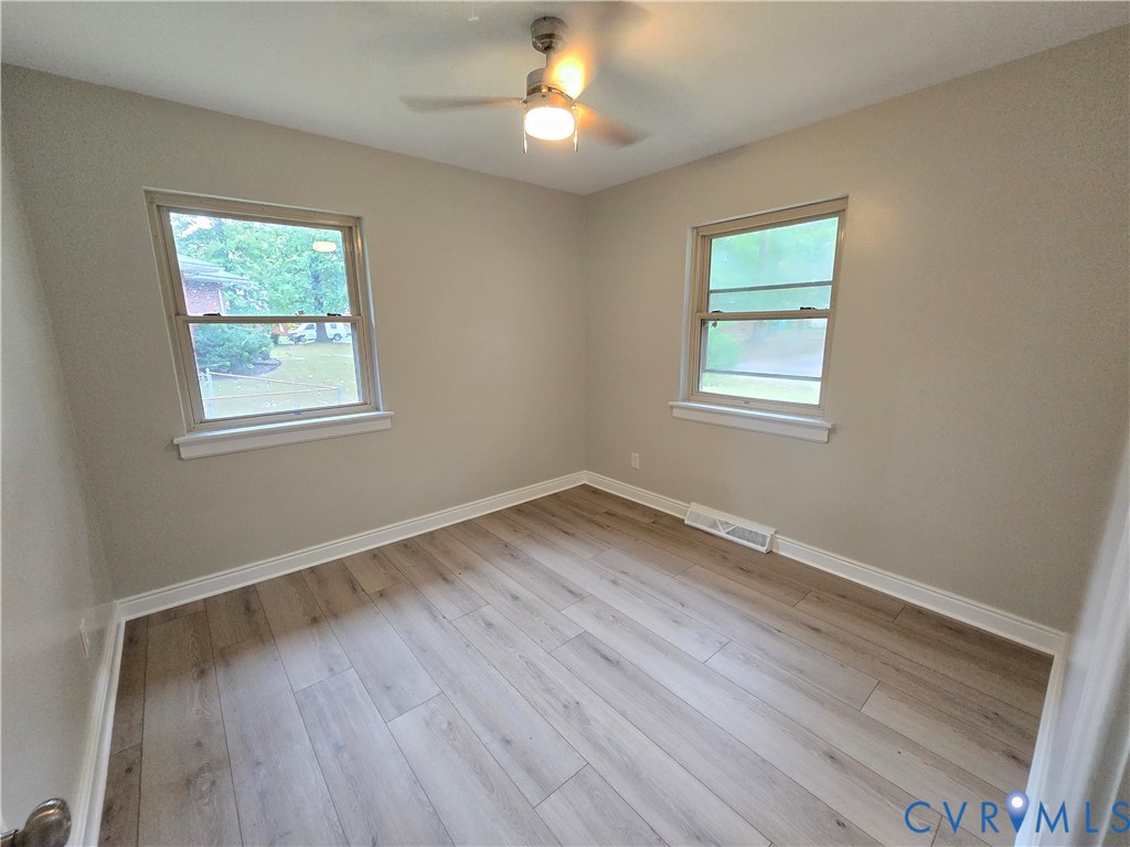 Primary bedroom with LVP flooring, two windows with natural light, and a central ceiling fan with an integrated light fixture