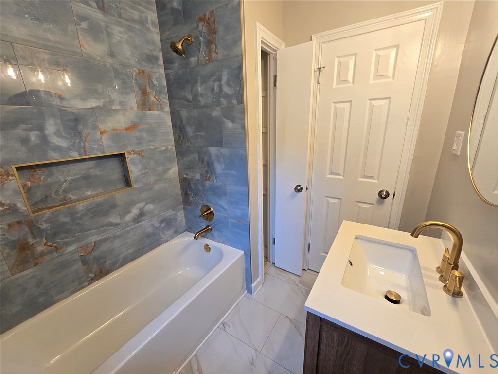 Bathroom featuring a deep soaking tub with blue-toned tile surround, integrated shower niche, gold-toned plumbing fixtures, and a vanity with a white countertop