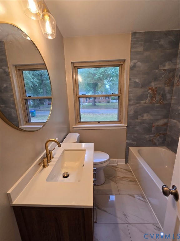 Bathroom featuring a vanity with a white rectangular sink and brass faucet, round wall-mounted mirror, large-format floor tiling, and a tiled tub surround