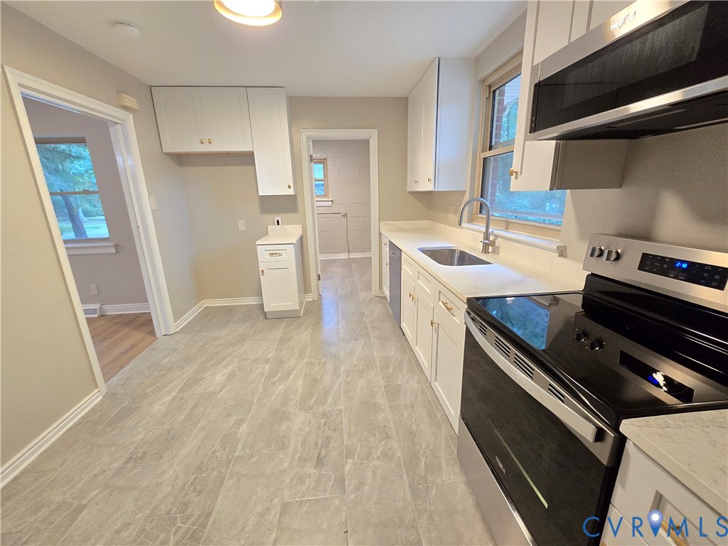 Kitchen featuring white shaker-style cabinetry, stone-surface countertops, tile flooring, stainless steel appliances, and a double-basin undermount sink