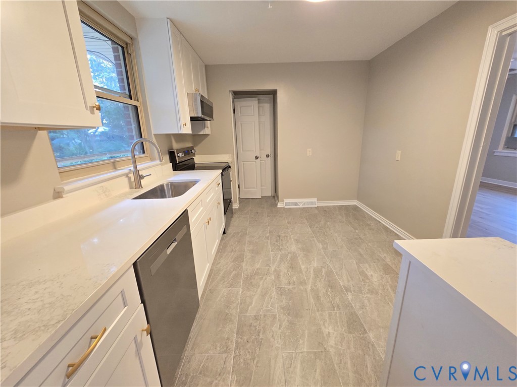 Kitchen featuring white cabinetry, solid surface countertops, stainless steel appliances, a gooseneck faucet, and stone-finish tile flooring