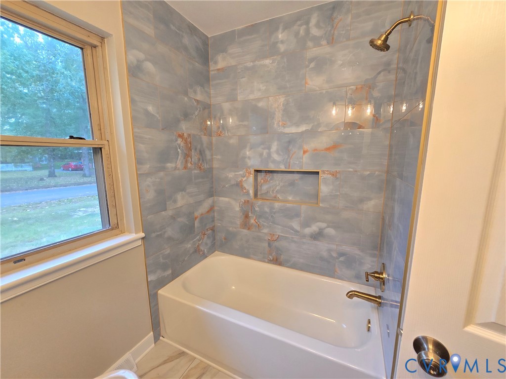 Bathtub surround featuring large-format tile with blue and copper veining, integrated wall niche, and metallic shower hardware