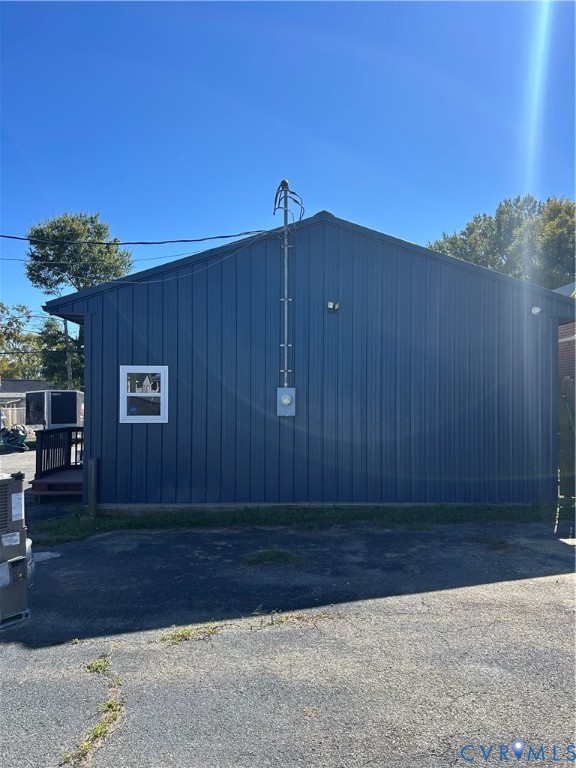 Exterior featuring dark blue vertical metal siding, an asphalt paved lot, and a white-framed window